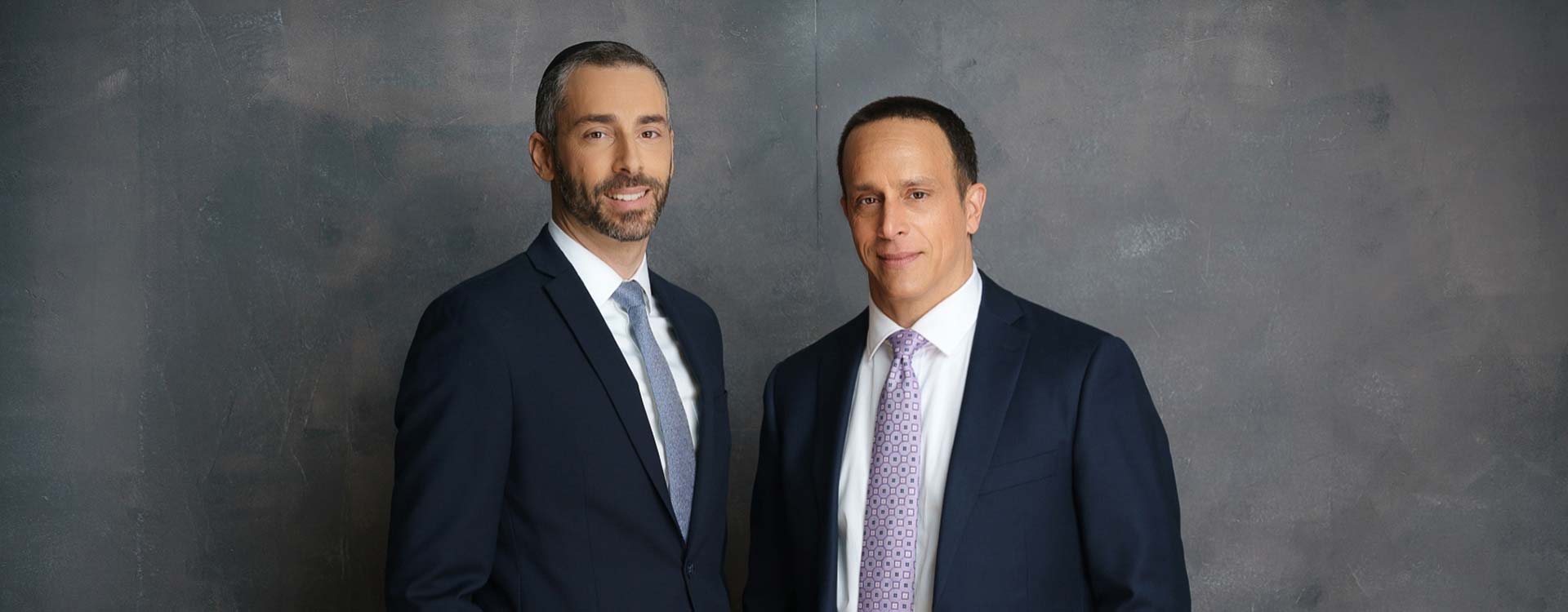 lawyers Joshua L. Kopple and Michael S. Kopple standing in front of a grey wall